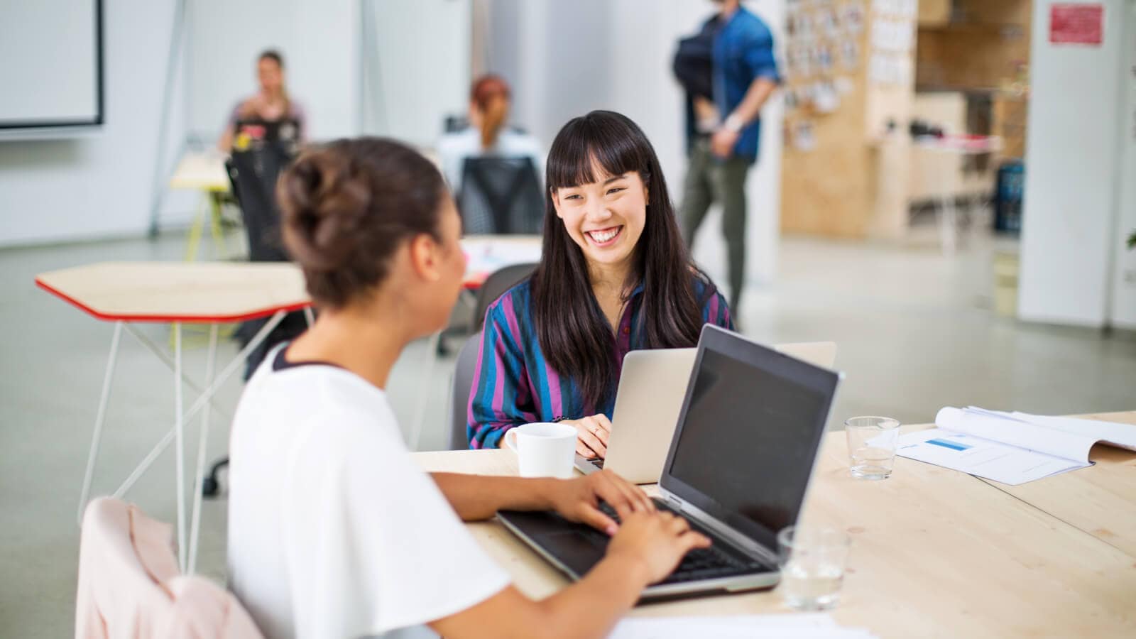 Young businesswomen working on laptops and smiling at table