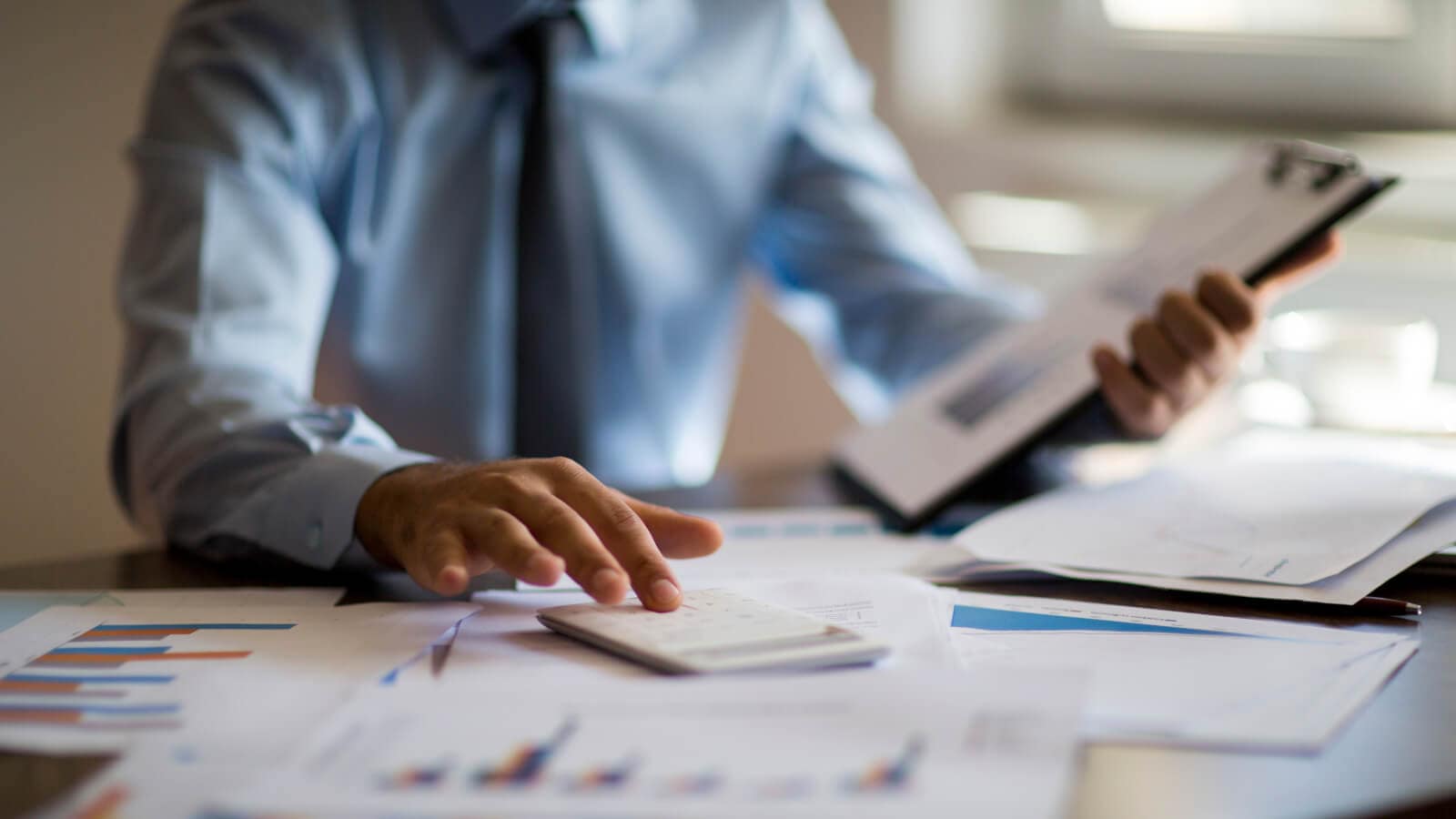 Business man using calculator with computer laptop, budget and loan paper in office