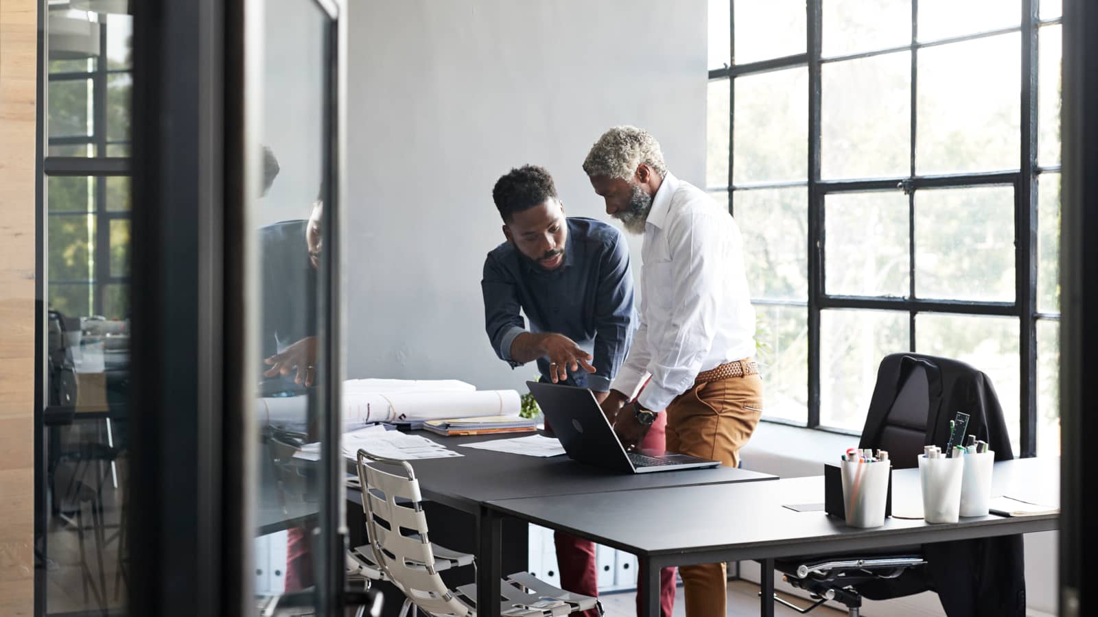 Entrepreneurs in a discussion while standing by desk in modern office seen through doorway