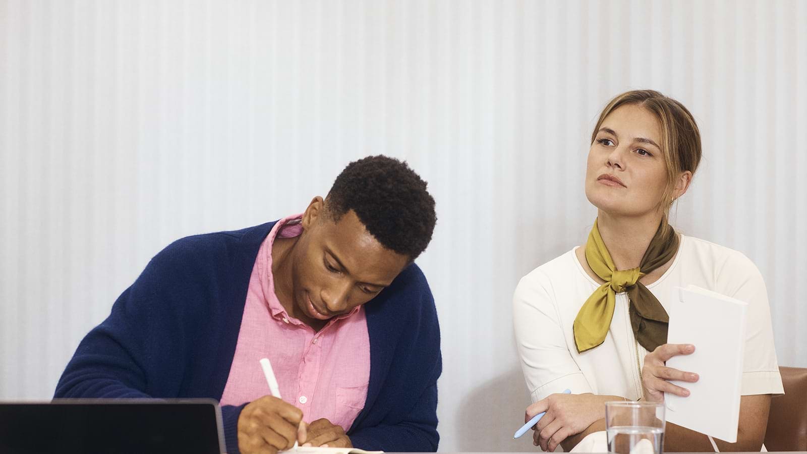 Two individuals taking notes during a professional meeting