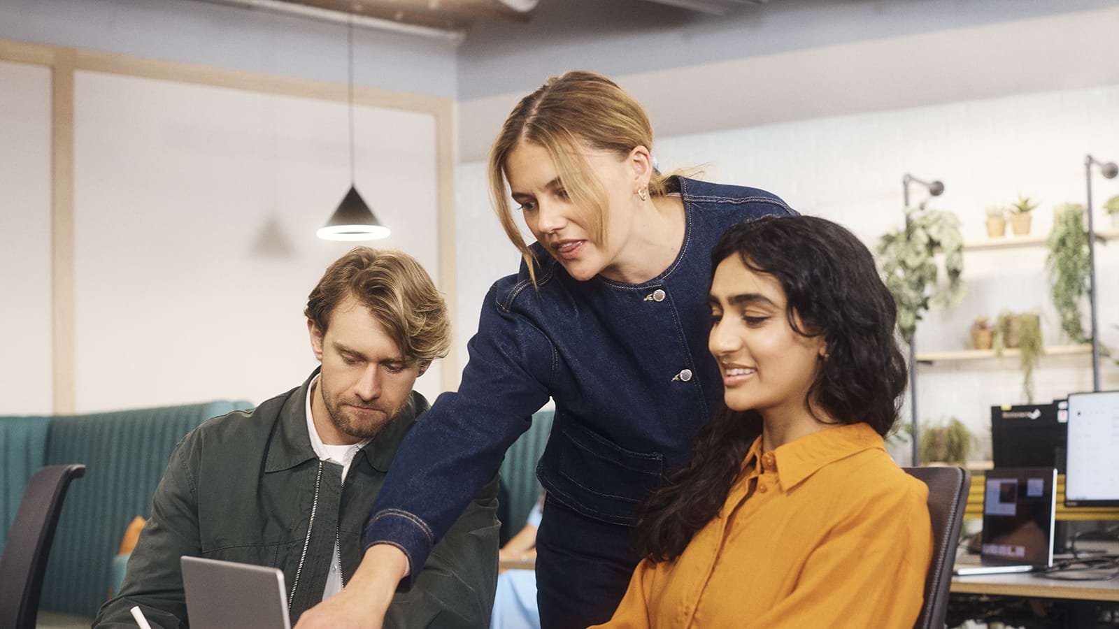 A group of colleagues working together with one woman pointing to a laptop screen