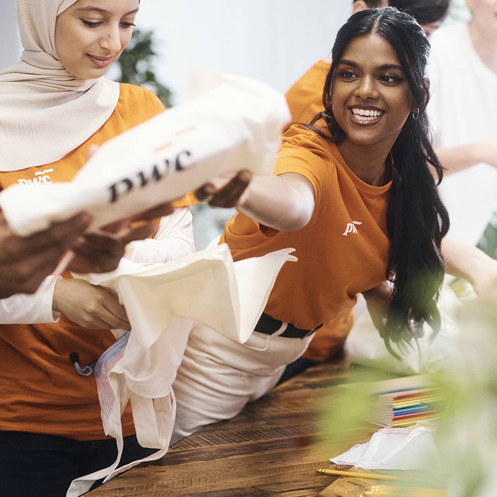 Volunteer handing out a PwC tote bag at a community event